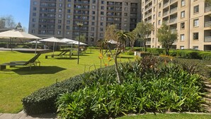 Un edificio residencial de gran altura con varios balcones, un césped bien cuidado y zonas de estar al aire libre.