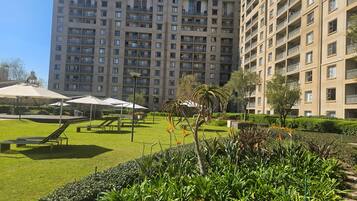 A high-rise residential building with multiple balconies, a well-maintained lawn, and outdoor seating areas.