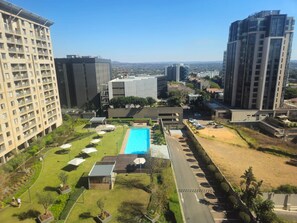 Um edifício alto com piscina no terraço e áreas verdes ao redor.