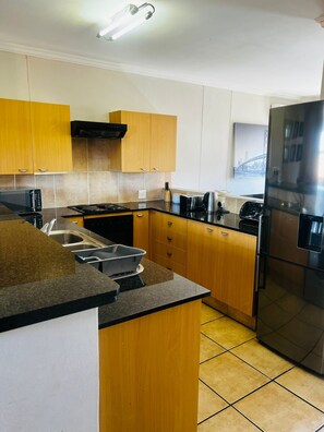 A modern kitchen with wooden cabinets, a stainless steel refrigerator, and a microwave. - Sandton Westpoint Luxury Apartments 158 (Sandton)