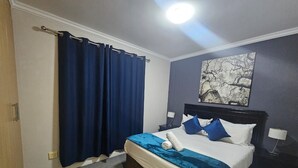 Et hotelværelse med en seng, et natbord, en lampe, et billede på væggen og et gardin.