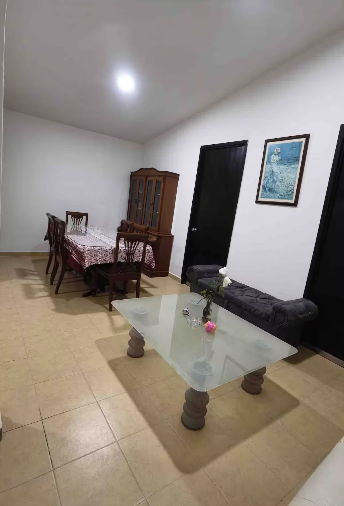 A dining area with a glass-top table, chairs, a cabinet, a sofa, and a door.