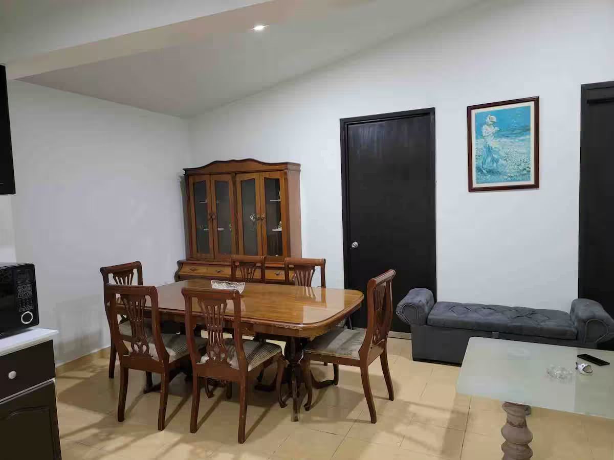 A dining area with a wooden table and chairs, a cabinet, a sofa, and a framed picture on the wall.