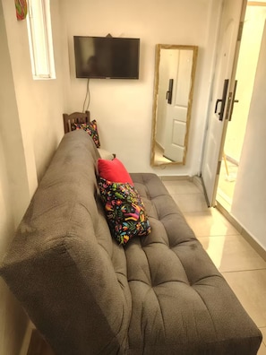 Ett vardagsrum med en soffa, en tv som är monterad på väggen och en dörr med en spegel.