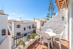 A terrace with white chairs and a table, overlooking a street with traditional buildings. - 2 Bedroom Apartment for Four Guests (Nerja)
