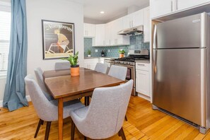 Eine moderne Küche mit weißen Schränken, einem Edelstahl-Kühlschrank und einem Essbereich mit Holztisch und grauen Stühlen.