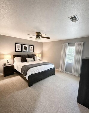 A bedroom with a bed, nightstands, a ceiling fan, and a window with curtains. - The Howdy Home | Near Texas A&M | Golf Course Views | Sleeps 10 (Bryan)