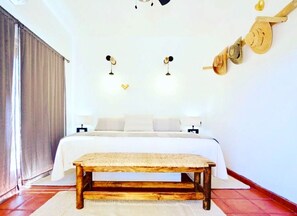 A bedroom with a bed, a bench, and a wall-mounted hat rack. - Private garden retreat 1-bedroom casita with AC in charming Sayulita (Sayulita)