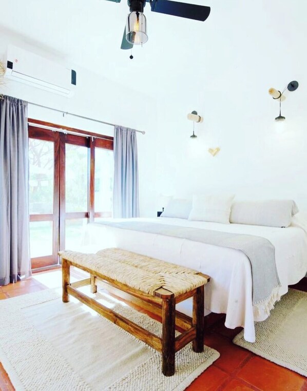 A bedroom with a large bed, a bench, a ceiling fan, and a view of the outdoors. - Private garden retreat 1-bedroom casita with AC in charming Sayulita (Sayulita)