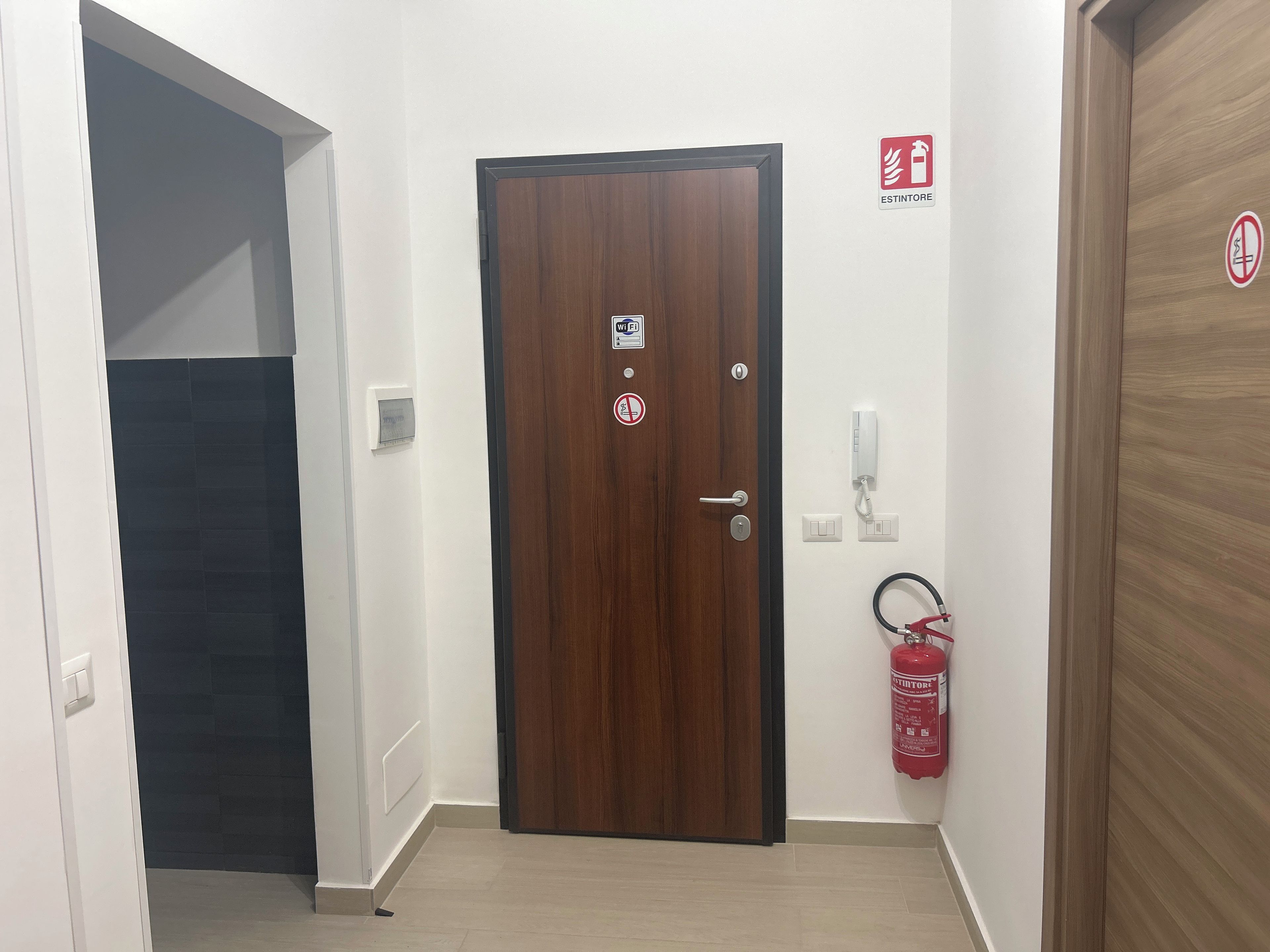 Un pasillo con una puerta de madera, un extintor y un letrero de Wi-Fi.