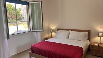 Una camera d'albergo con un letto, due comodini, una finestra con tende e vista sull'esterno.