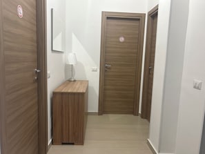 Um corredor com portas de madeira, uma mesa pequena com abajur e um interruptor na parede.