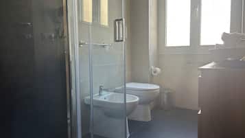 A bathroom with a glass shower enclosure, a toilet, and a bidet.