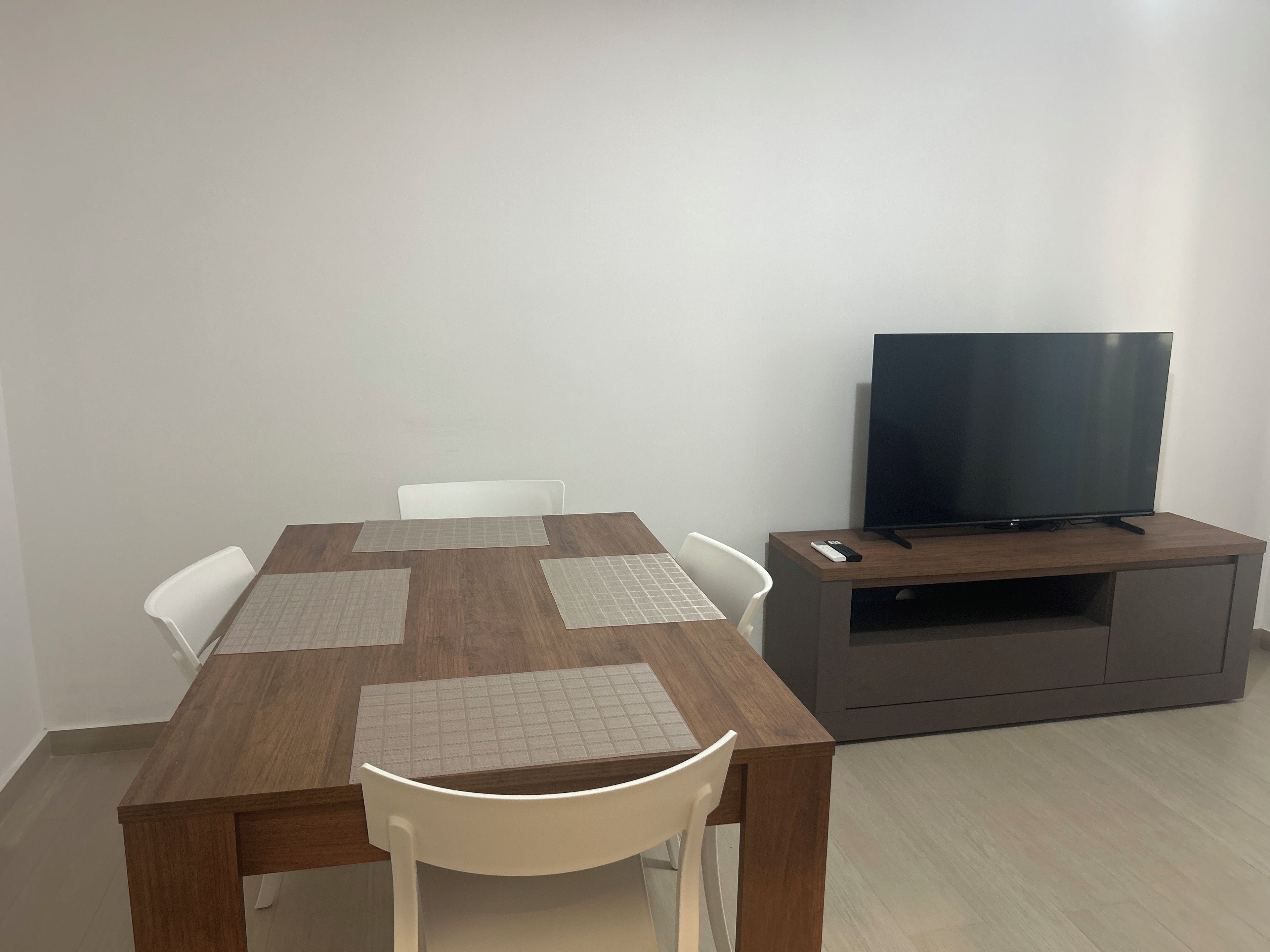 A dining table with four chairs, a television on a stand, and a remote control on the stand.