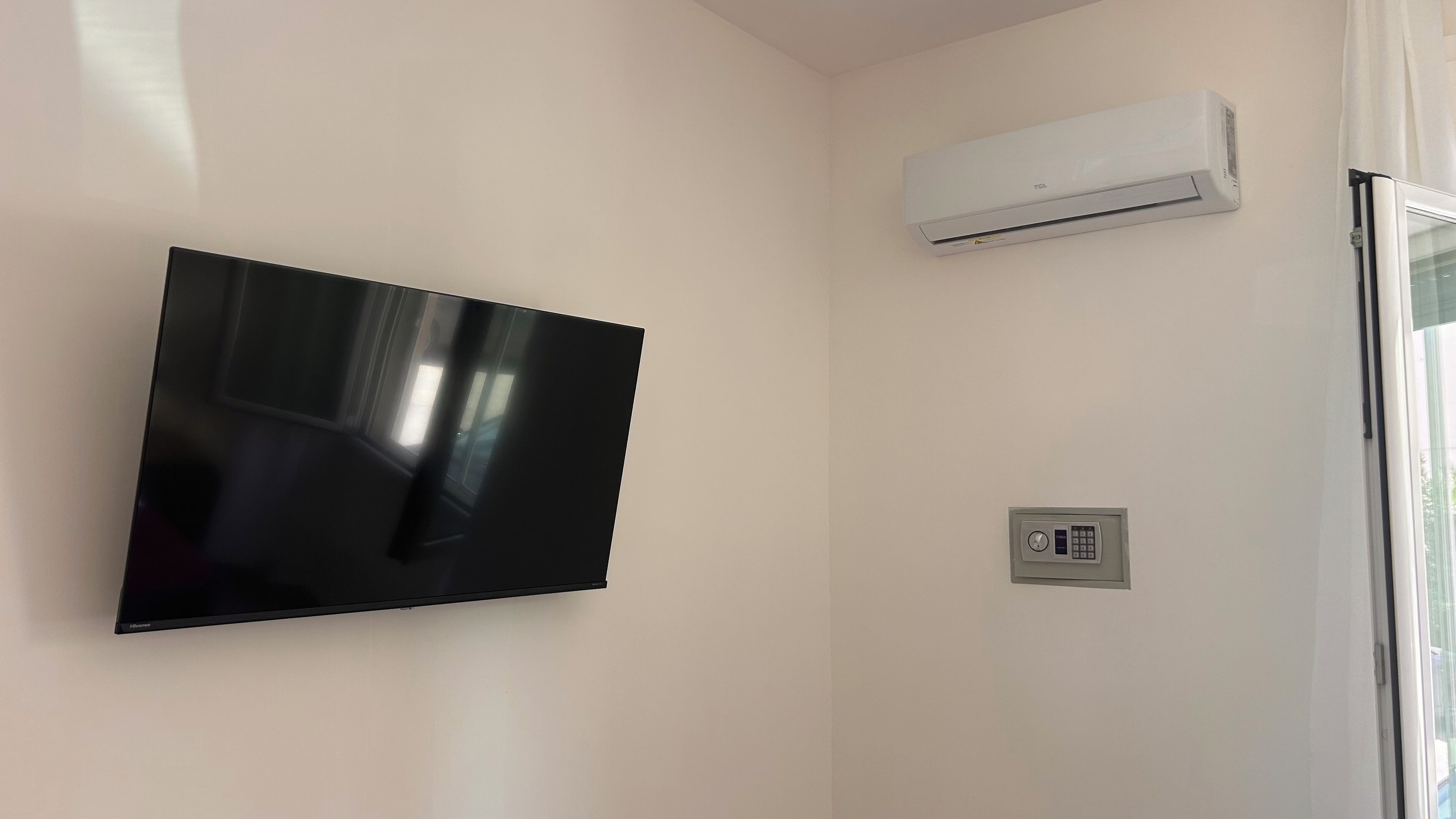A room with a mounted flat-screen TV, an air conditioning unit, and a security panel.