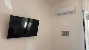 Quarto com televisão de tela plana montada, aparelho de ar condicionado e painel de segurança.