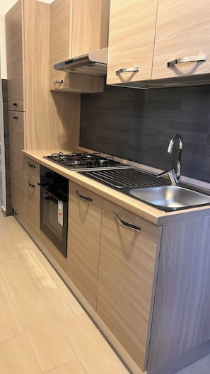 A modern kitchen with wooden cabinets, a stainless steel sink, and a built-in dishwasher. - Casa Surace: Your Stay Just a Stone's Throw from the Beach and the Central Station (Reggio Calabria)