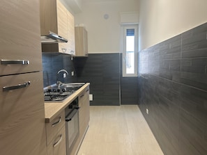 Una cocina moderna con armarios de madera, una campana extractora de acero inoxidable, un horno empotrado y un salpicadero de azulejos negros.