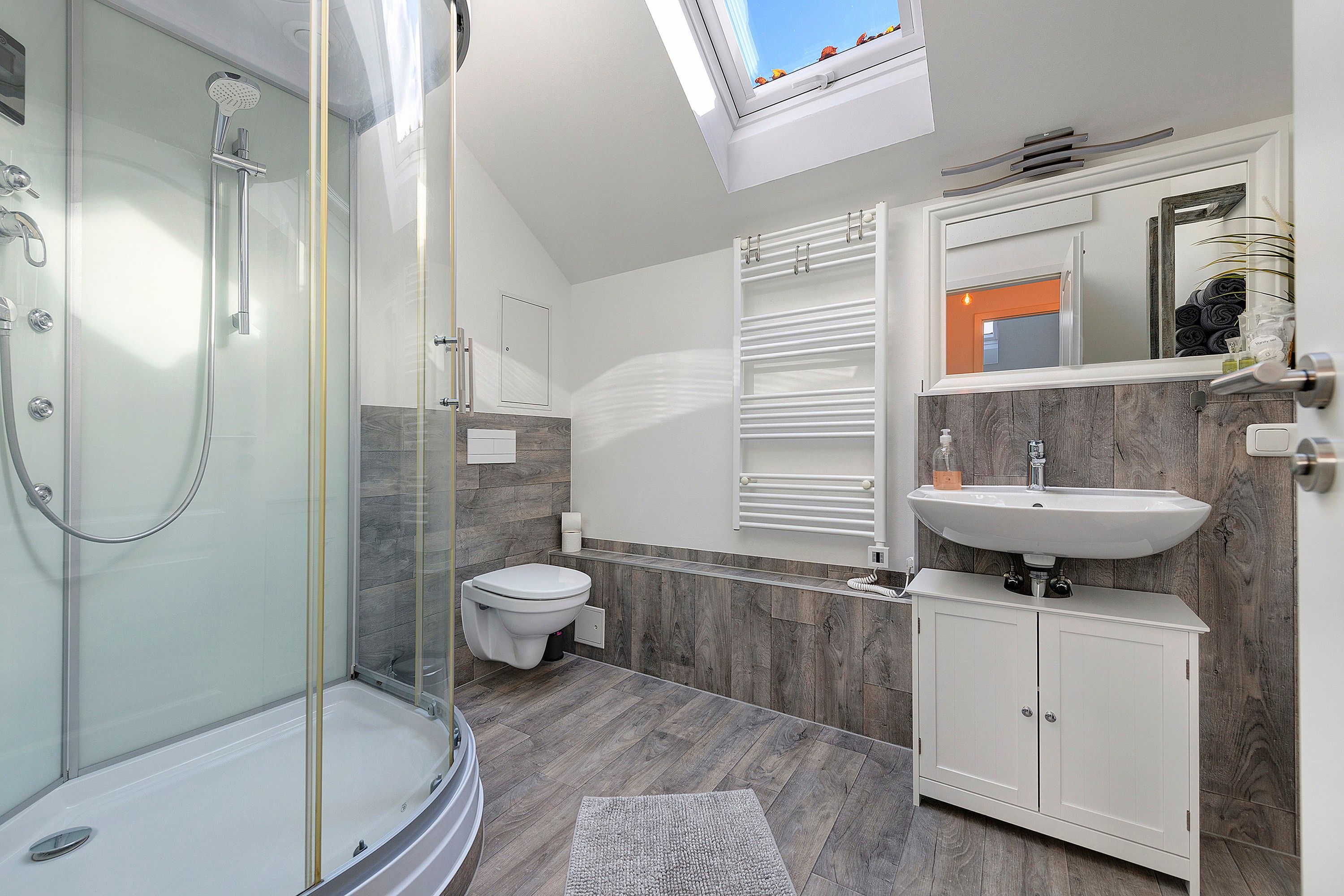Un baño moderno con ducha acristalada, inodoro, tocador con lavabo y espejo.