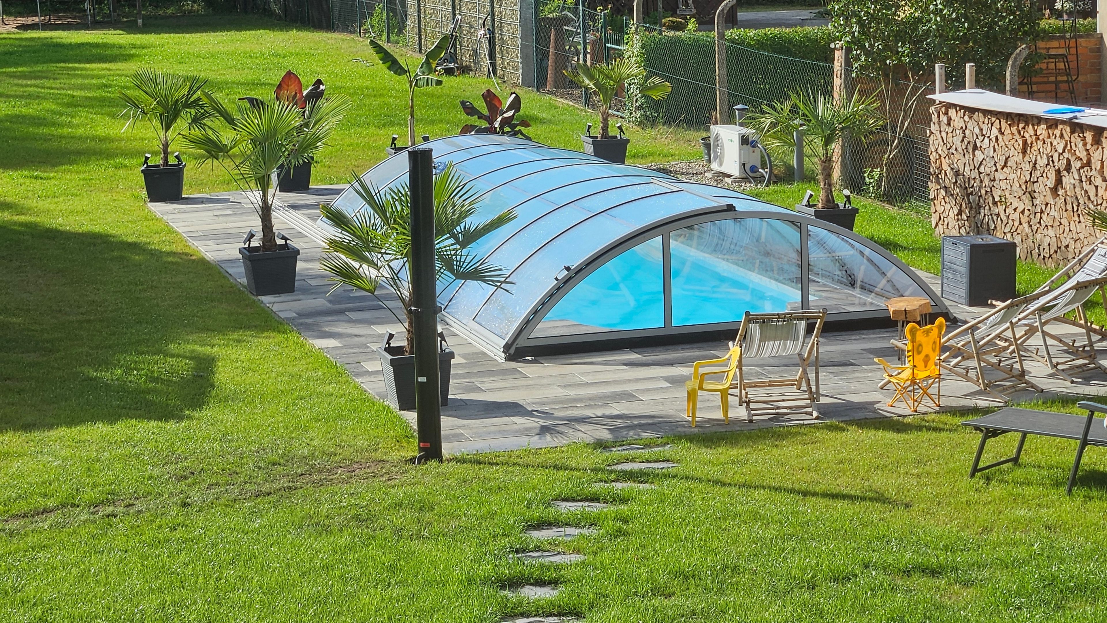 Una piscina con un recinto in vetro, circondata da un patio con sedie e un'amaca.