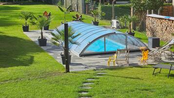 Una piscina con un recinto in vetro, circondata da un patio con sedie e un'amaca.