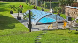 A swimming pool with a glass enclosure, surrounded by a patio with chairs and a hammock.