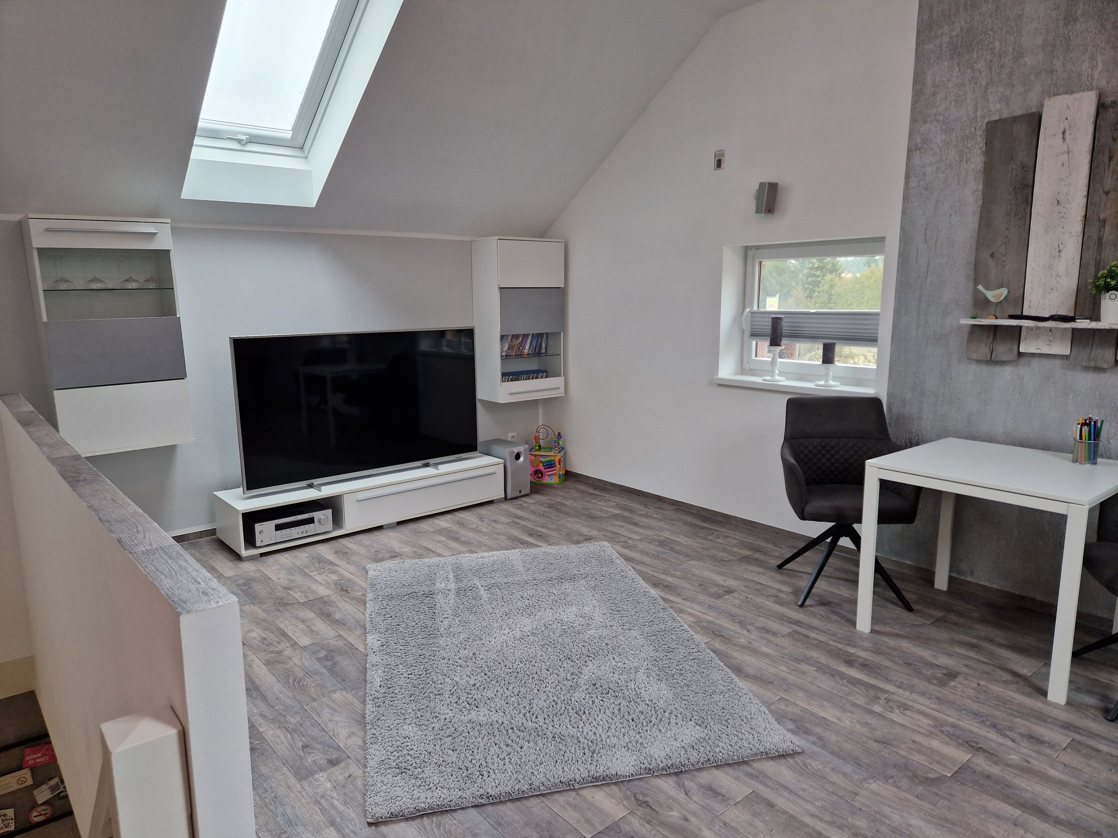 A modern living room with a flat-screen TV, a white table, and a grey carpet.