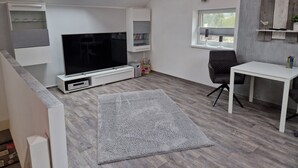 A modern living room with a flat-screen TV, a white table, and a grey carpet. - Holiday Home 'Ferienhaus in Fürstensee Wald See' with Shared Pool, Private Terrace and Wi-Fi (Neustrelitz)