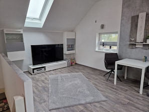 Ein modernes Wohnzimmer mit einem Flachbildfernseher, einem weißen Tisch und einem grauen Teppich.
