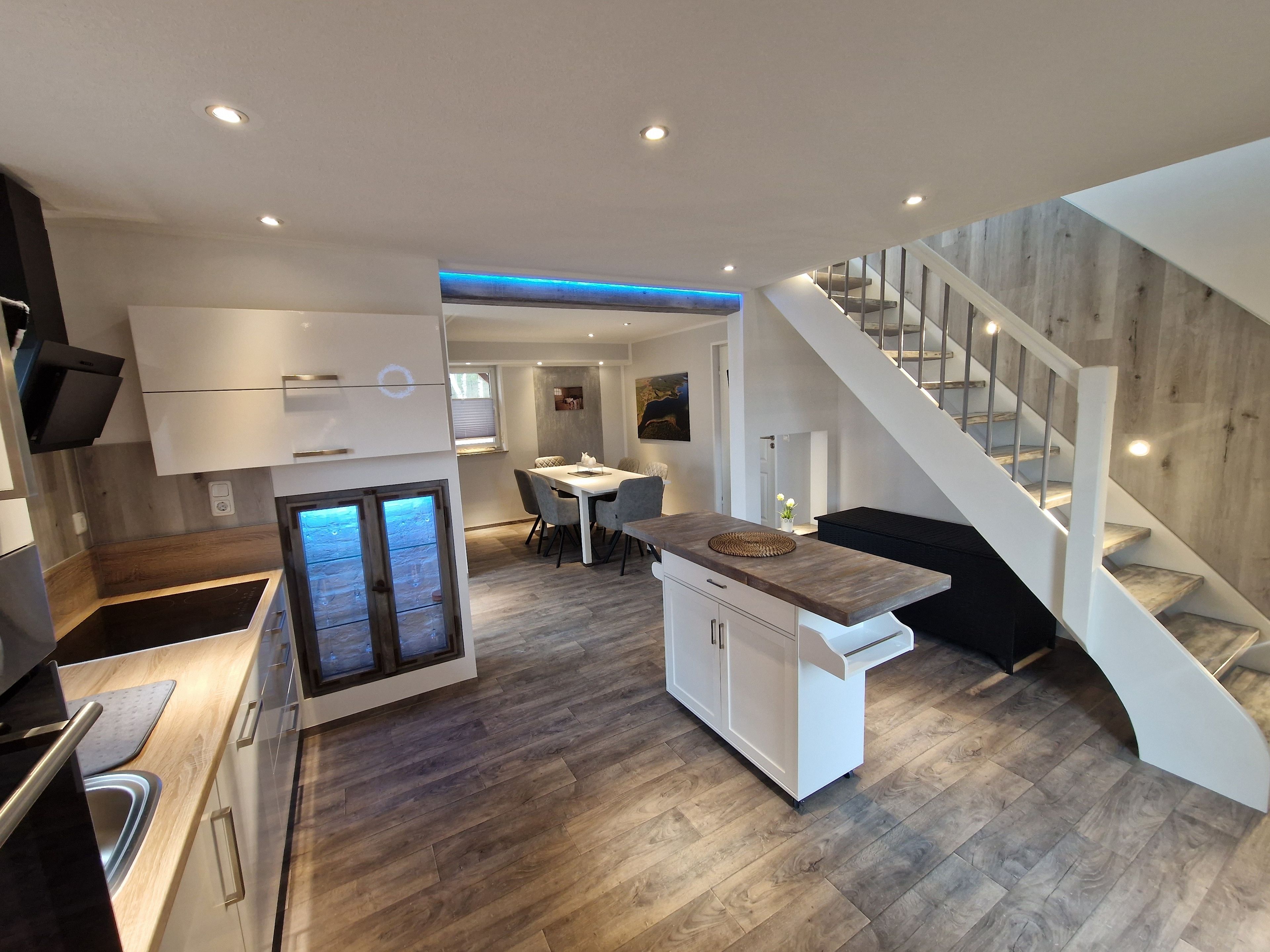 A modern kitchen with a built-in oven, a dining area with a table and chairs, and a staircase with a wooden finish.