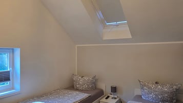 A small, well-lit attic bedroom with two beds, a window, and a skylight.