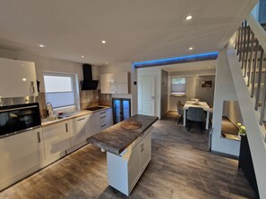 A modern kitchen with a central island, built-in appliances, and a dining area with a staircase.