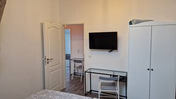 A bedroom with a bed, a desk with a chair, a television, and a wardrobe.