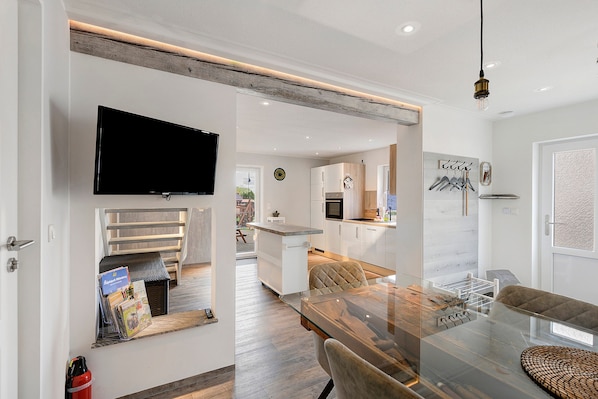 A modern kitchen with white cabinets, a built-in oven, and a dining area with a glass table and chairs.