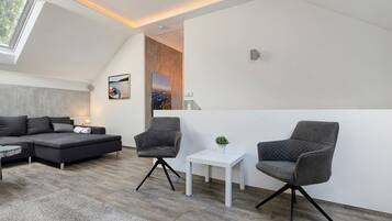 Ein modernes Wohnzimmer mit einer Couch, zwei Sesseln, einem kleinen Tisch und einem Gemälde an der Wand.