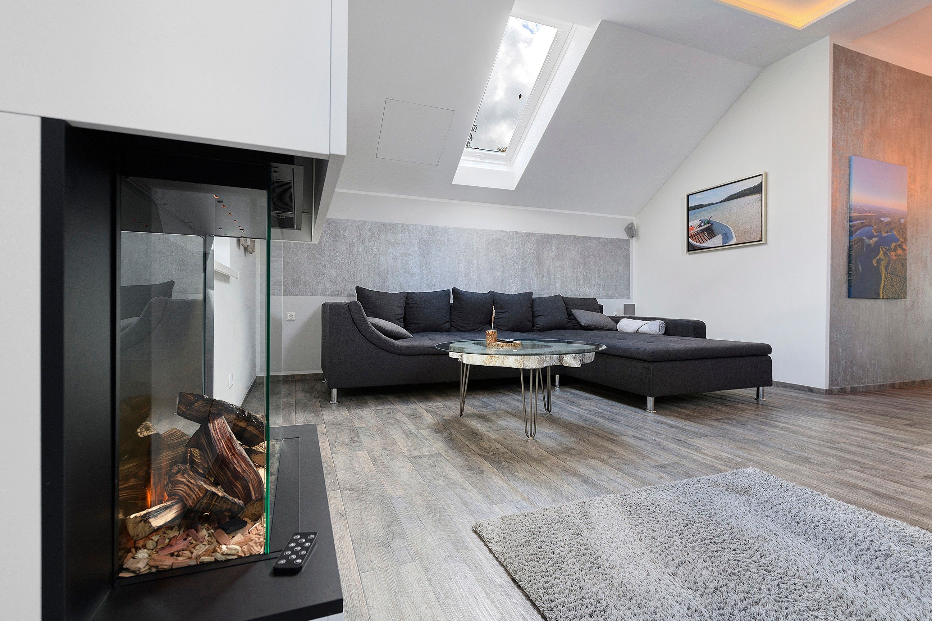 Ein modernes Wohnzimmer mit einer Eckcouch, einem Glastisch und einem Kamin mit brennendem Holzfeuer.
