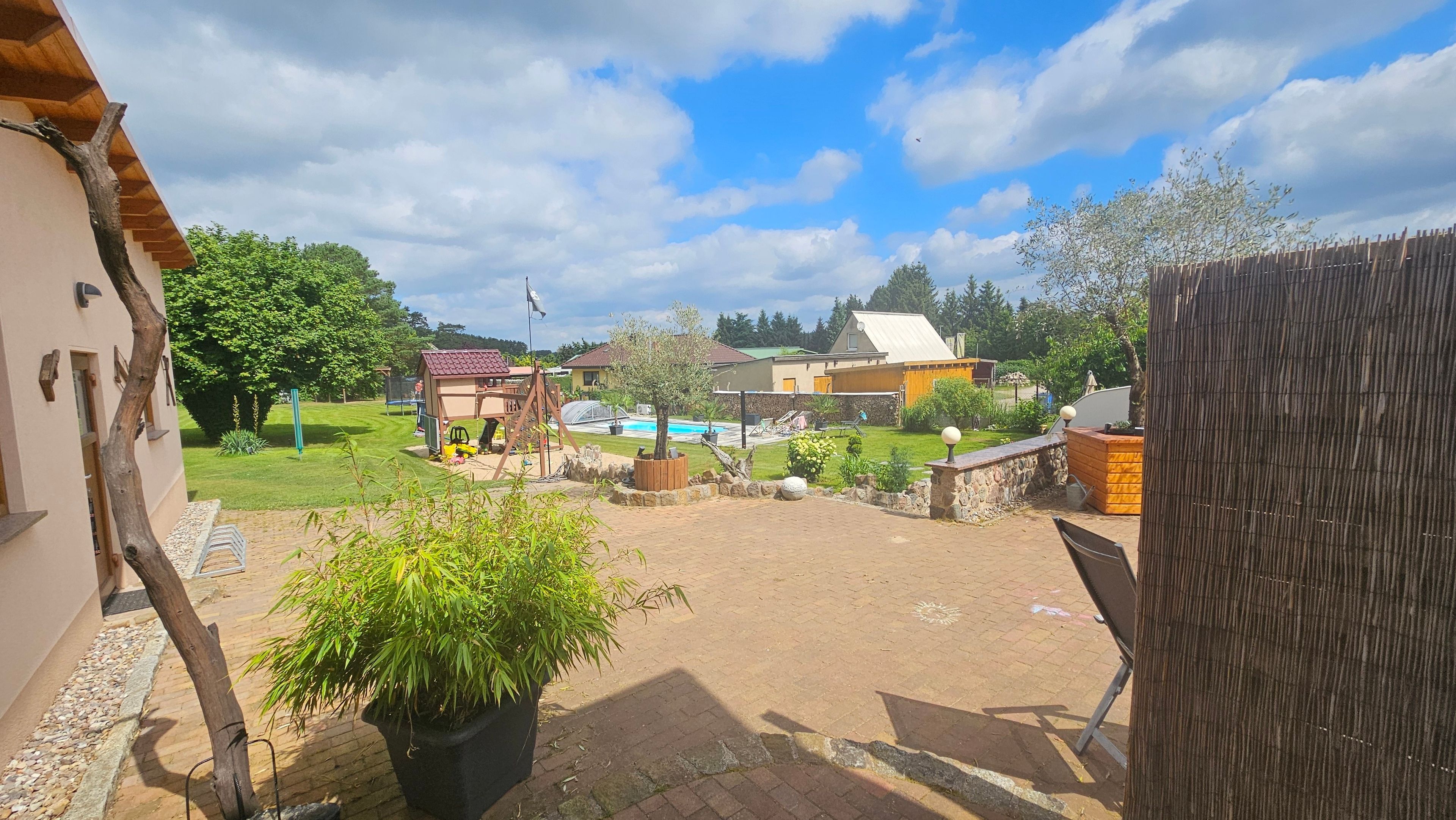 A residential backyard with a swimming pool, a wooden playhouse, and a garden area.