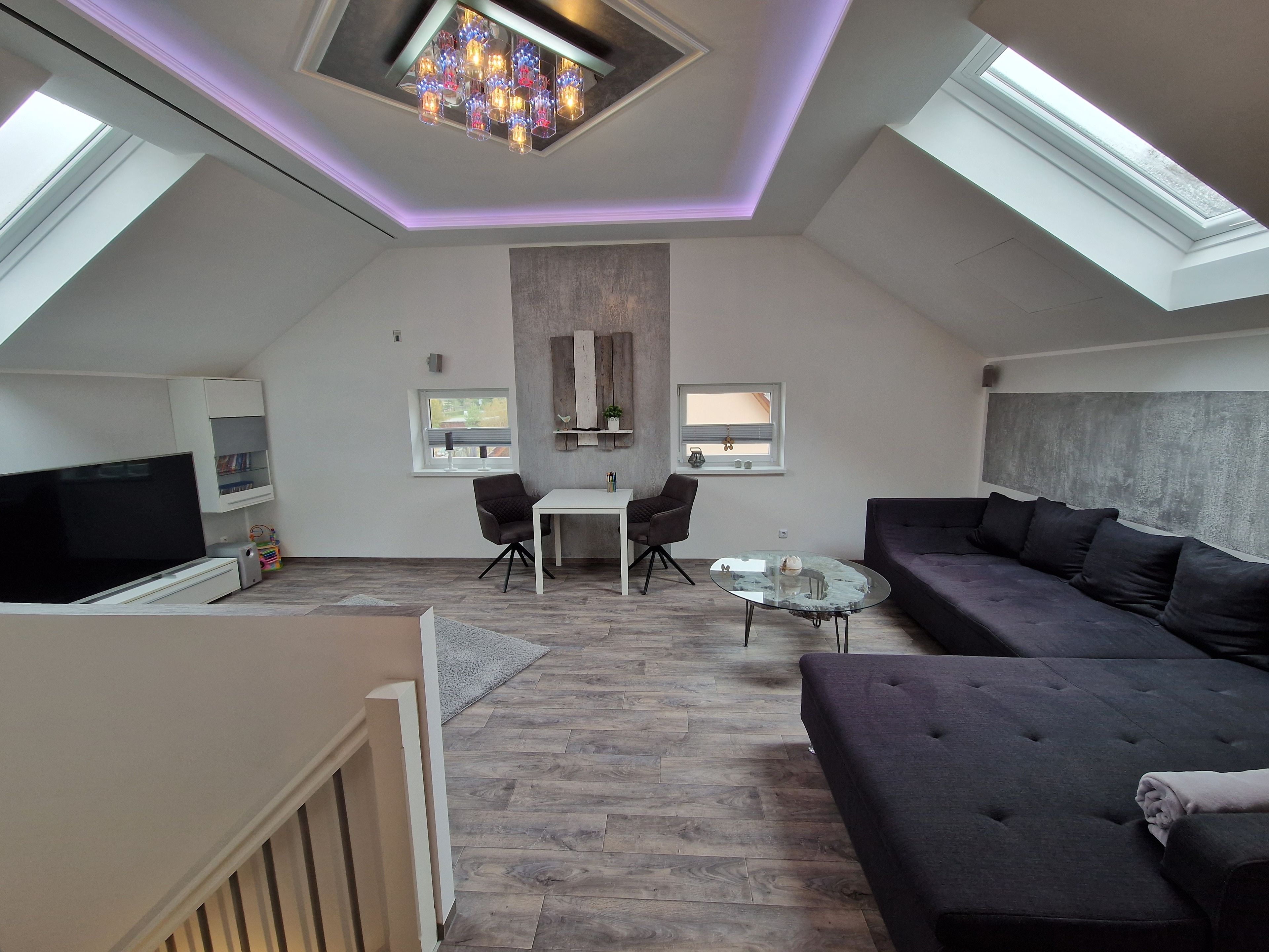 Ein modernes Loft-Apartment mit hohen Decken, Dachfenstern, einem Flachbildfernseher, einer Couch, einem Esstisch und einer kleinen Küchenzeile.
