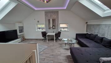 Ein modernes Loft-Apartment mit hohen Decken, Dachfenstern, einem Flachbildfernseher, einer Couch, einem Esstisch und einer kleinen Küchenzeile.