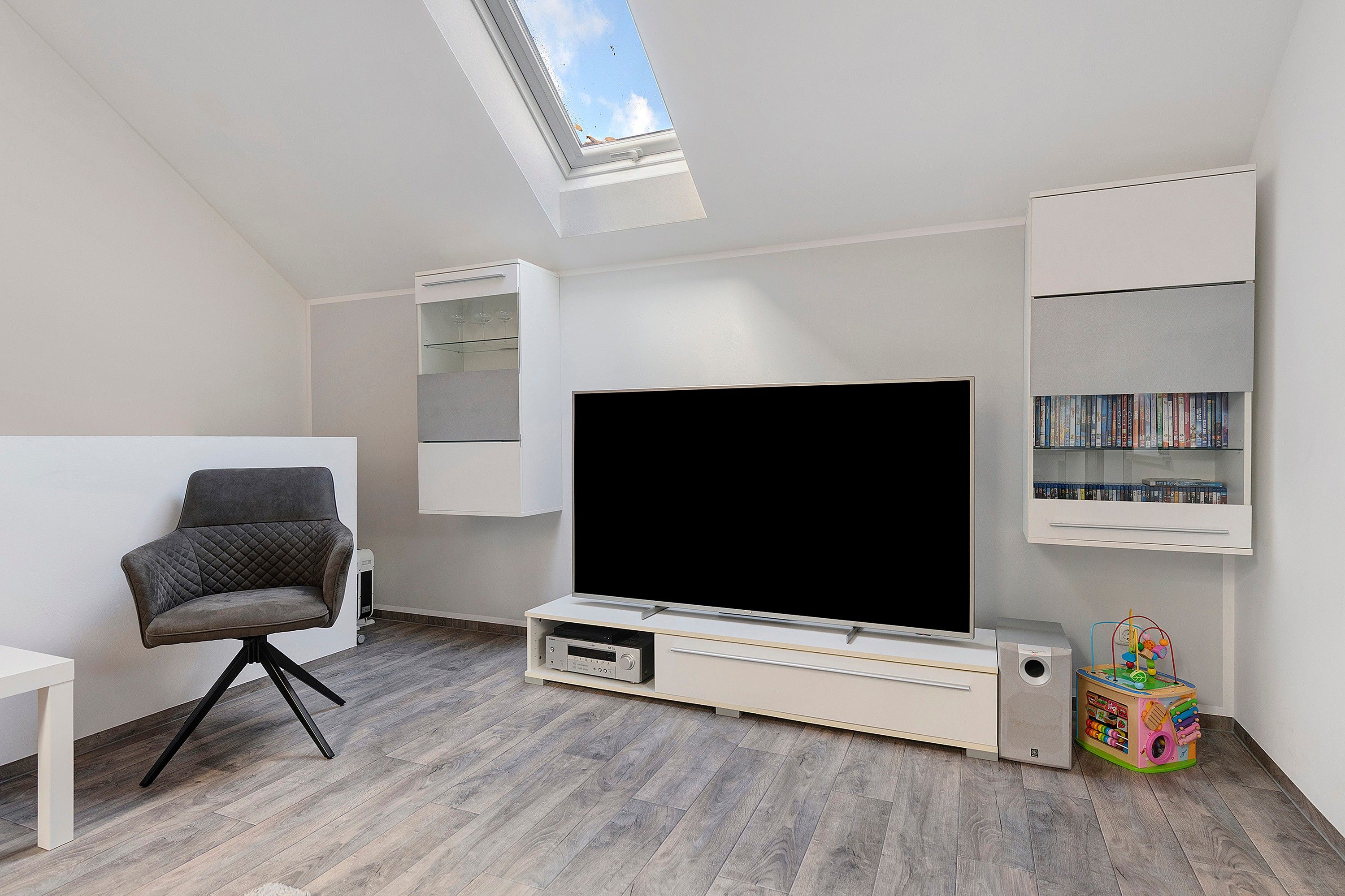 Ein modernes Wohnzimmer mit Fernseher, Bücherregal, Spielzeug und einem Oberlicht.