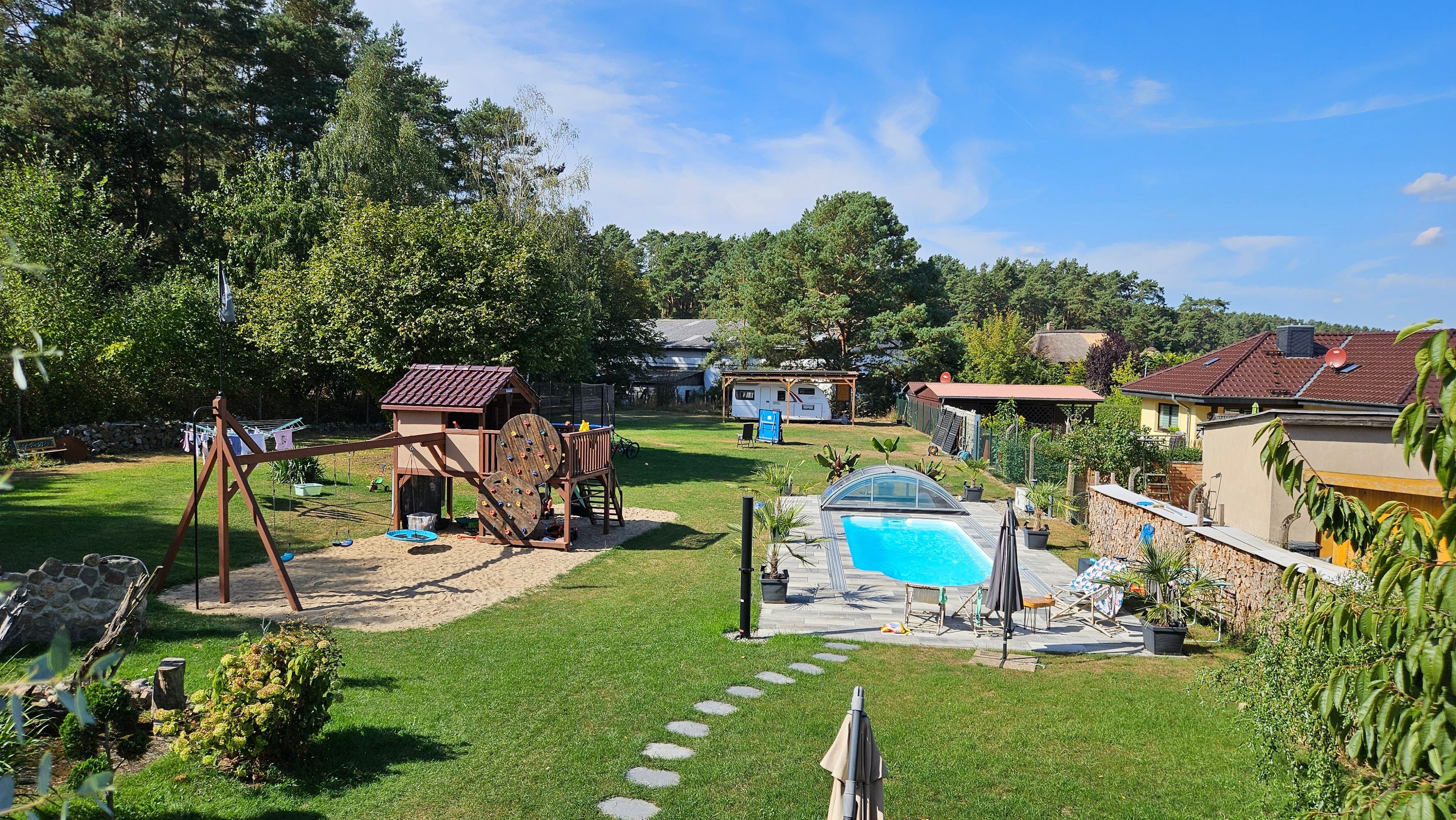 Ein Garten mit Schaukel, einem kleinen Spielhaus, einem Swimmingpool und einer Steinmauer.