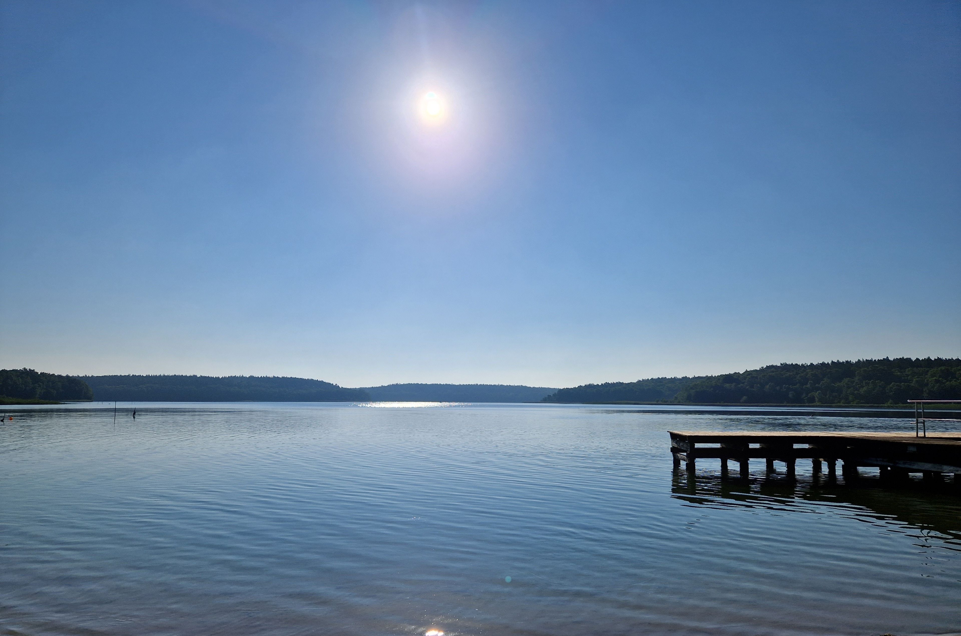 A calm lake with a wooden dock extending into the water, surrounded by forested hills.