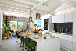 A modern kitchen with a large island, pendant lighting, and a view to the outdoors. - Maison Sylvie  Résidence Maracuja Orient Bay (Orient bay)