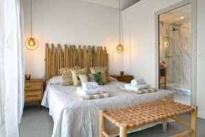 A neatly arranged bedroom with a bed, bedside tables, a bench, and a shower area. - Maison Sylvie  Résidence Maracuja Orient Bay (Orient bay)