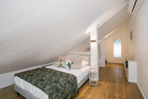 A bedroom with a sloped ceiling, a bed with a patterned bedspread, a bedside table with a lamp, and a window providing natural light. - Maison Sylvie  Résidence Maracuja Orient Bay (Orient bay)