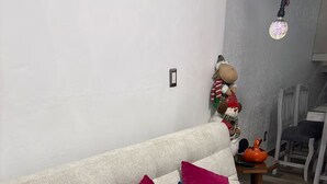 Een bank met twee kussens, een klein tafeltje met een vaas en een afstandsbediening, en een decoratief object aan de muur.
