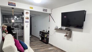 Een woonkamer met een bank, een flatscreen-televisie aan de muur en een visgraatparketvloer.