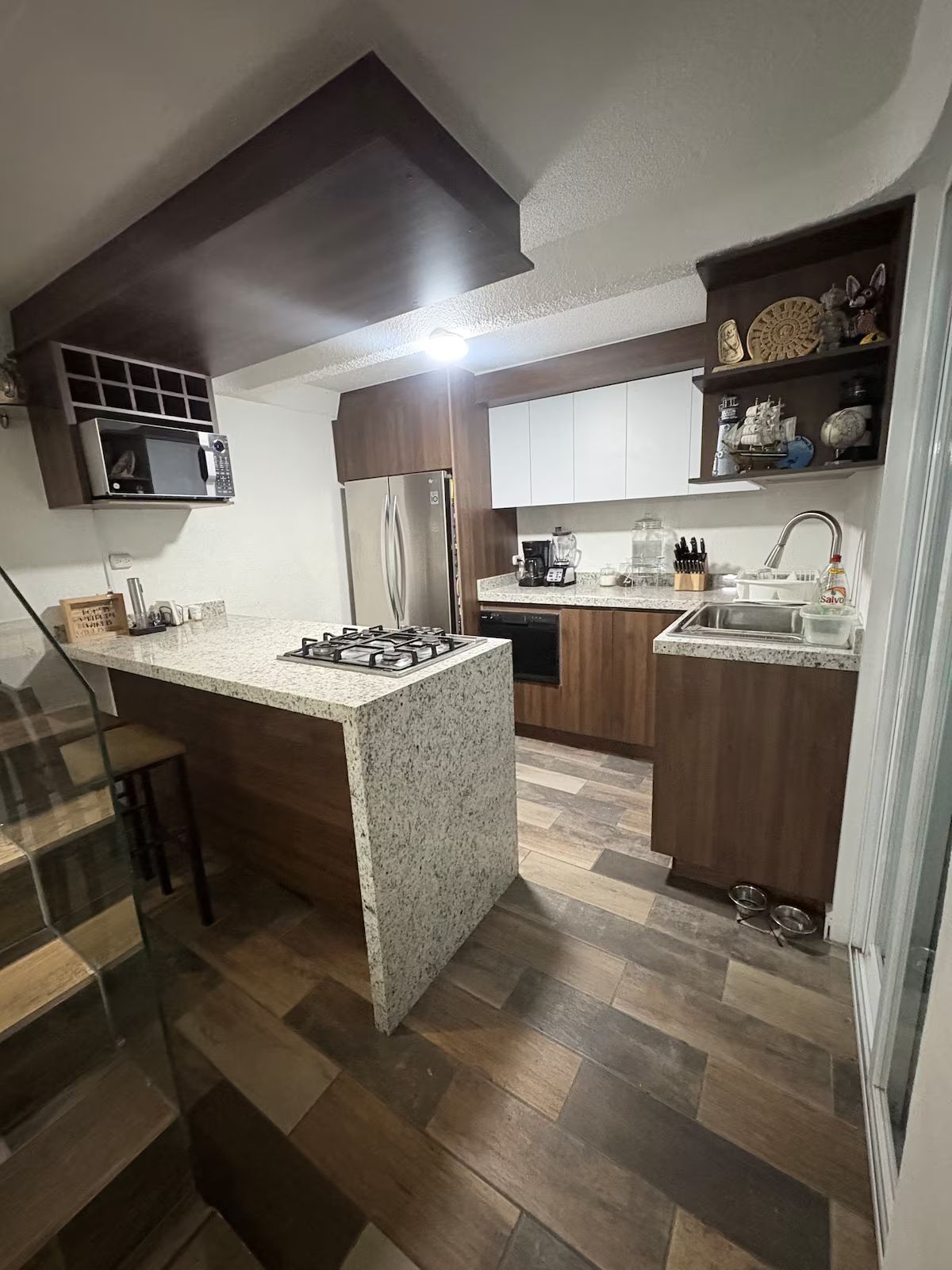 Une cuisine moderne dotée d’un îlot central, d’appareils électroménagers intégrés et d’un plancher en bois.