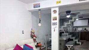 Een woonkamer met een bank, kussens, een decoratieve lamp en een keuken in de achtergrond.