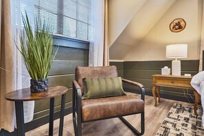 Ein Zimmer mit Ledersessel, einem kleinen runden Tisch mit Topfpflanze, einem Nachttisch aus Holz mit Lampe und einem gemusterten Teppich.